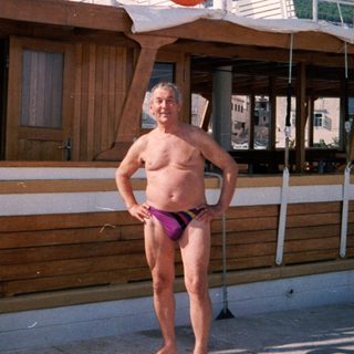 Shirtless man in swim trunks posing near lifebuoy on boat.