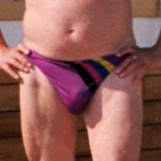 Shirtless man in swim trunks posing near lifebuoy on boat.