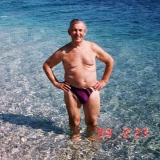 Shallow coastal scene with man standing in water near seaside village.