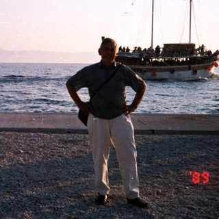 Man standing by seaside pier with boat in background.