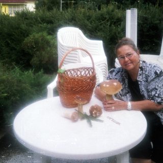 Woman sitting at outdoor table with basket, drink, and flowers.
