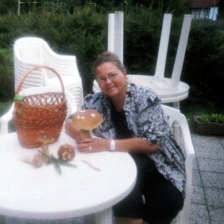 Woman sitting at outdoor table with basket, drink, and flowers.