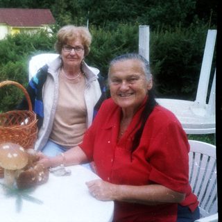 Two elderly women smiling outdoors by a table with basket.