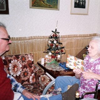 Two people in a cozy room, one holding gift-wrapped box.
