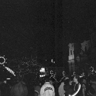Nighttime crowd celebrating with fireworks near illuminated clock tower.