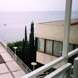 Coastal view with building, sea, boat, and cypress tree.