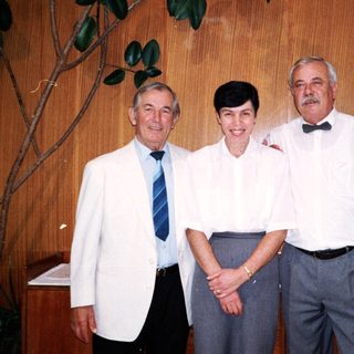 Three adults posing together indoors in formal attire.