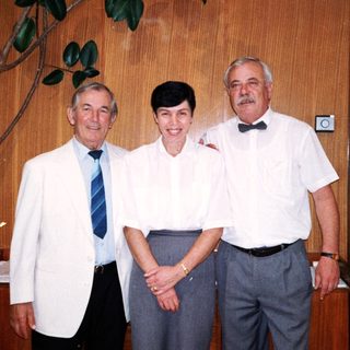 Three adults posing together indoors in formal attire.