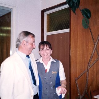 Two people smiling indoors near a door.