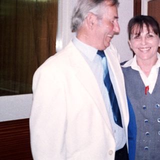 Two people smiling indoors near a door.