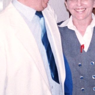 Two people smiling indoors near a door.