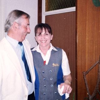Two people smiling indoors near a door.