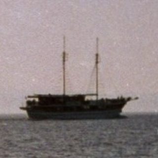 Boat sailing on calm ocean under twilight sky.