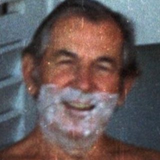 Shirtless man sitting in chair waving.