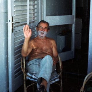Shirtless man sitting in chair waving.