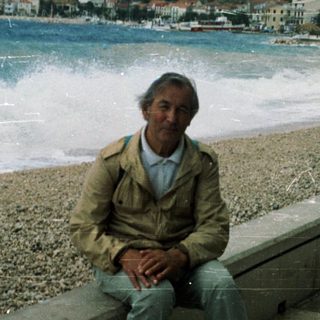 Man sitting on seaside bench by pebble beach.