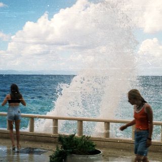 Two women enjoying ocean water fountain by seaside.