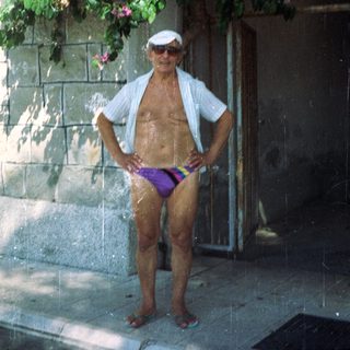 Older man in swim trunks posing outdoors.
