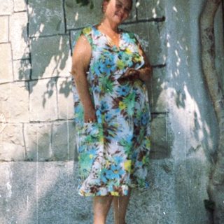Woman in floral dress posing near blooming wall.