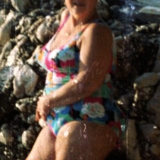 Woman standing in shallow coastal waters near rocks.