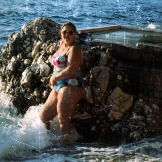 Woman standing in shallow coastal waters near rocks.