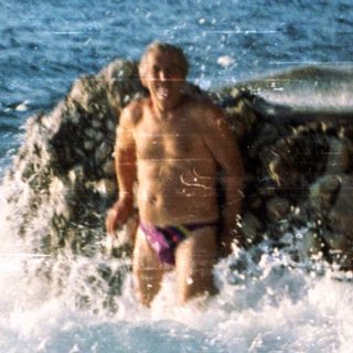 Person swimming near rocky coastal jetty.