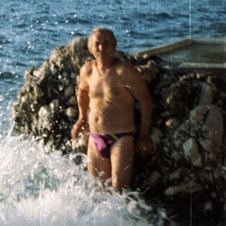 Man sitting on rocks by ocean waves.