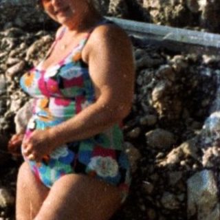 Woman in swimwear by rocky seaside pool.