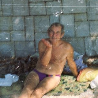 Showering man in outdoor brick-walled bath area.