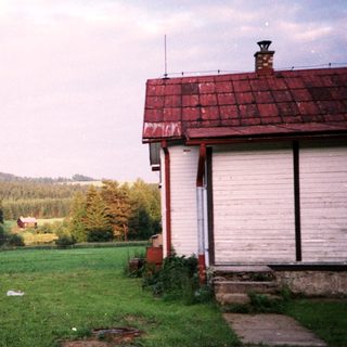 Rural scene with small houses, open fields, and distant hills.