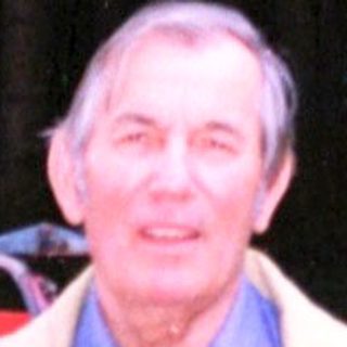 Man standing beside red cart in forested area.