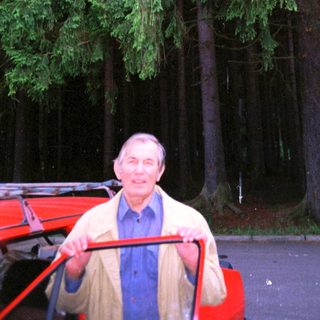 Man standing beside red cart in forested area.
