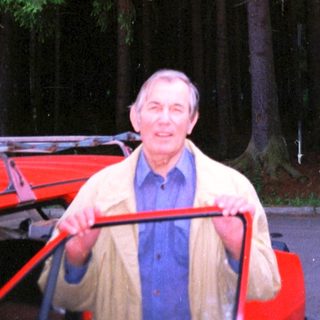 Man standing beside red cart in forested area.