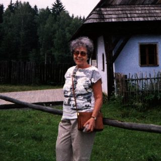 Traditional wooden house with steep roof, woman posing outside.