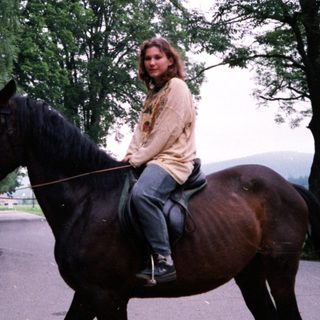 Woman riding horse on country road.