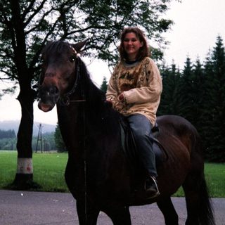 Woman riding black horse on paved path.