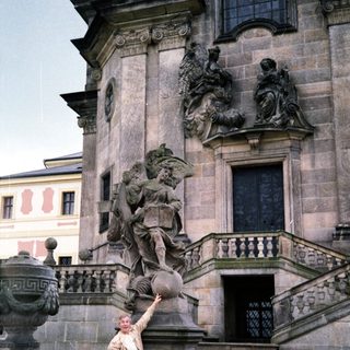 Man posing beside Baroque-style statue in courtyard.