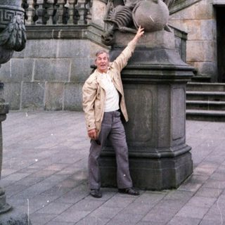 Man posing beside Baroque-style statue in courtyard.
