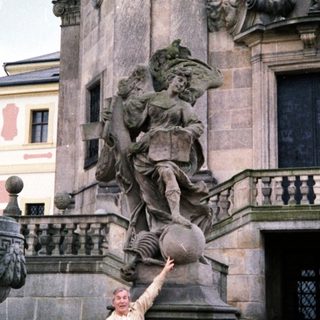 Man posing beside Baroque-style statue in courtyard.