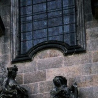 Man posing beside Baroque-style statue in courtyard.