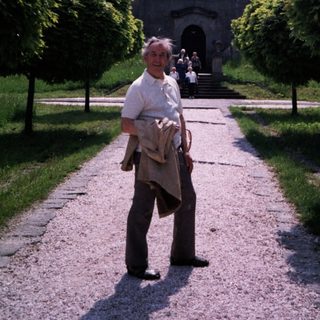 Man walking toward historic stone gate in landscaped park.