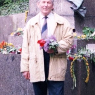 Man posing with floral wreath at historic monument.
