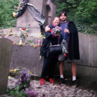 Two people posing with statue surrounded by floral tributes.