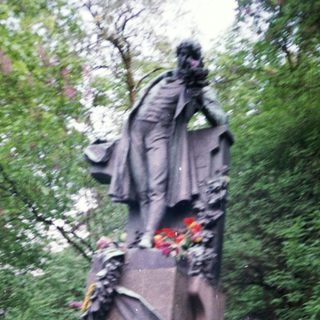 Two people posing with statue surrounded by floral tributes.