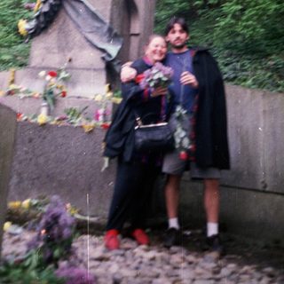 Two people posing with statue surrounded by floral tributes.