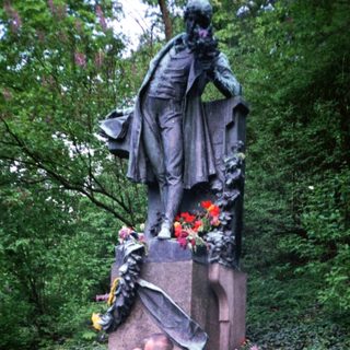 People paying respects at a memorial statue with flowers.