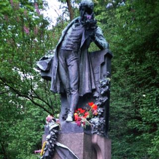 People paying respects at a memorial statue with flowers.