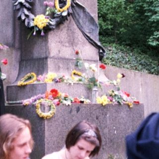 Memorial statue with floral tributes and visitors.