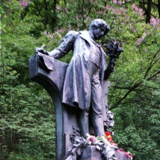 Memorial statue with floral tributes and visitors.