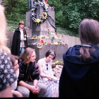 Memorial statue with floral tributes and visitors.